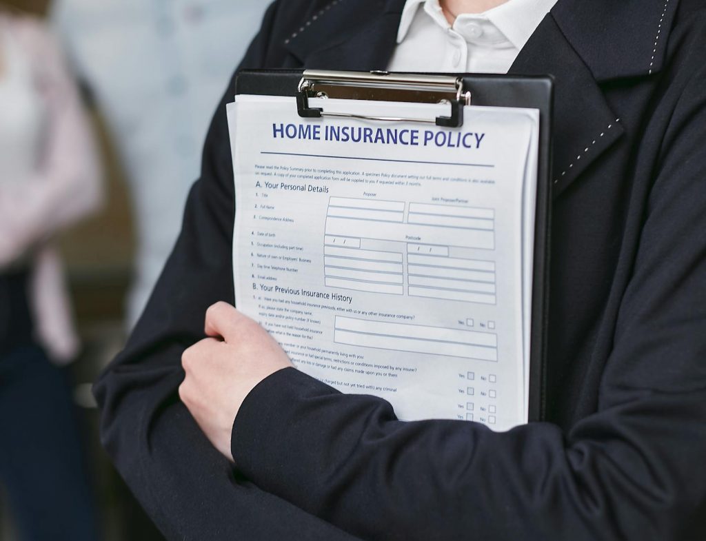 A person holding an umbrella over a house, car, and other belongings.